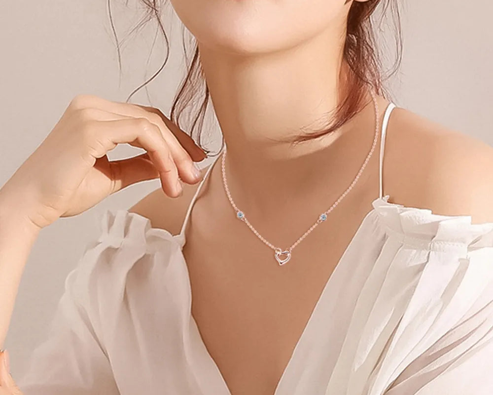 NEWYORKLISTED Valentine’s Day Specials: Woman wearing a delicate necklace with a heart design against a neutral background