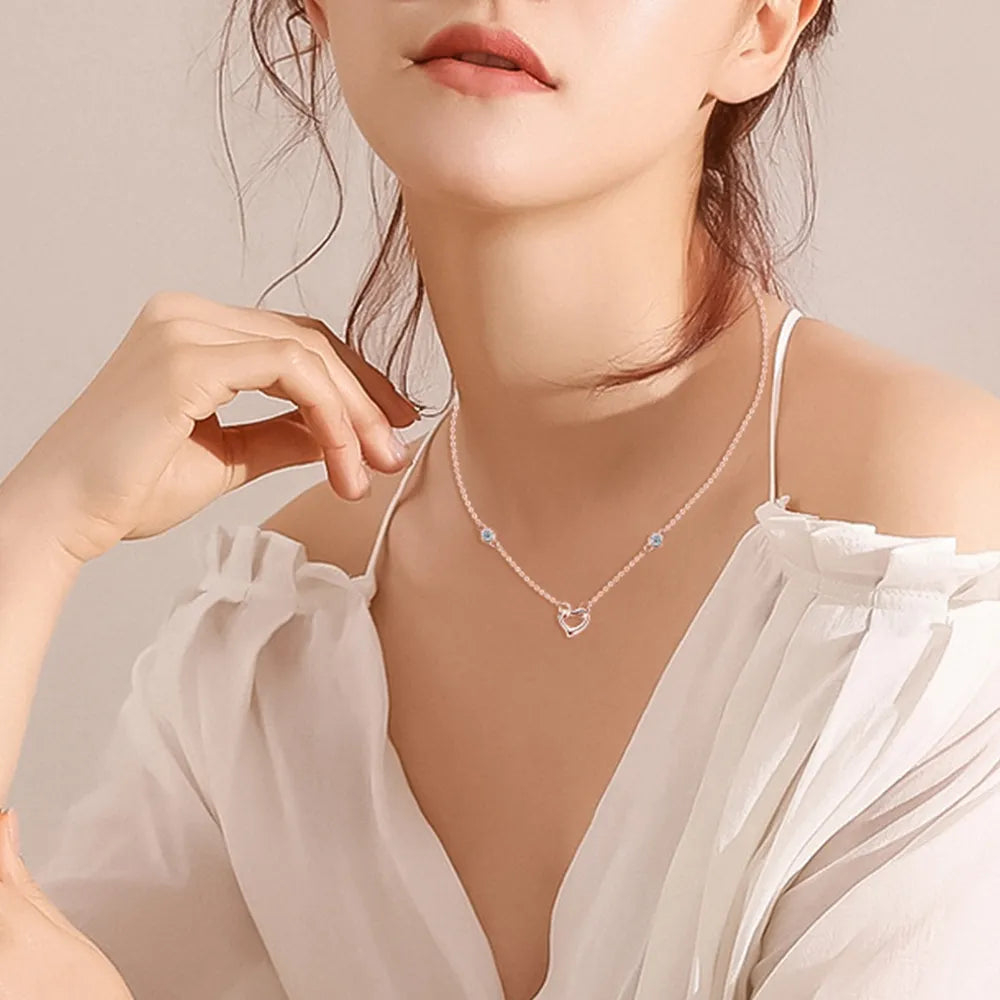 NEWYORKLISTED Valentine’s Day Specials: Woman wearing a delicate necklace with a heart design against a neutral background