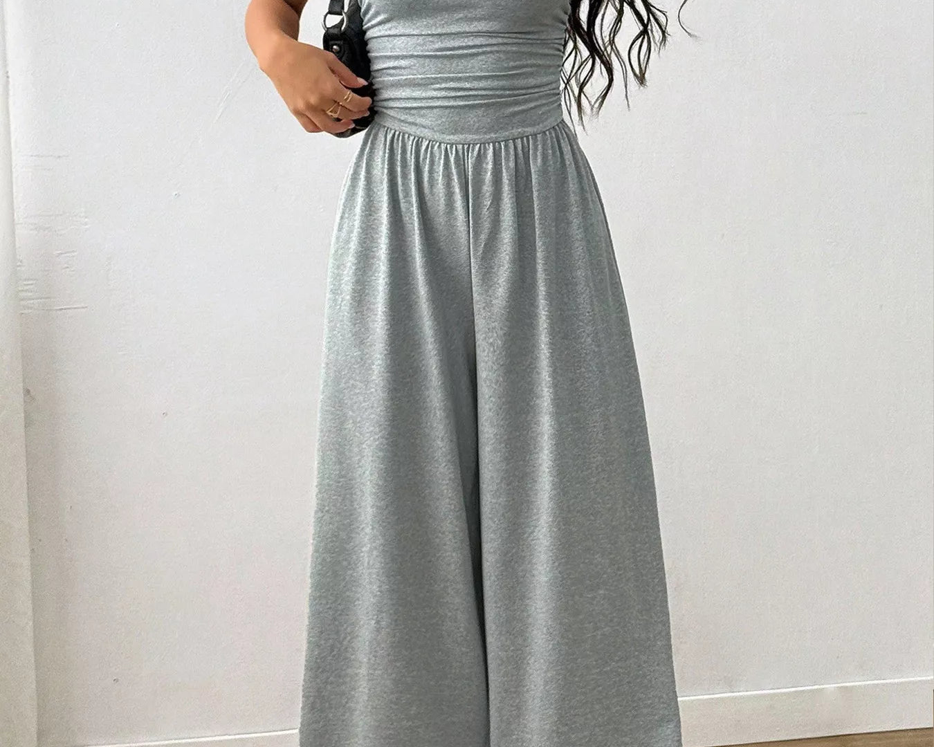 NEWYORKLISTED Comfort Collection: Woman wearing a gray jumpsuit against a white wall.