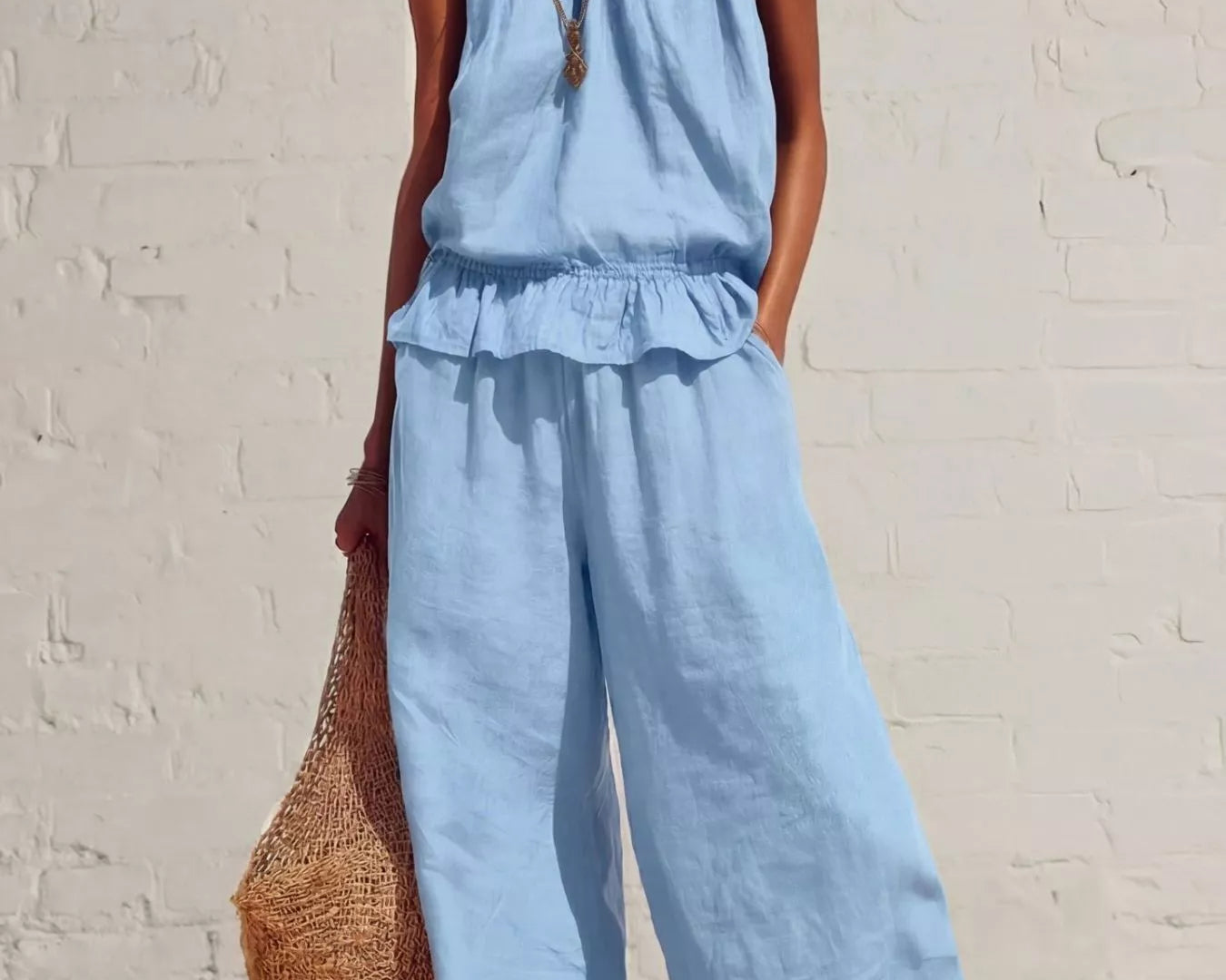 NEWYORKLISTED STYLE COLLECTION: Woman wearing a light blue jumpsuit against a white brick wall.