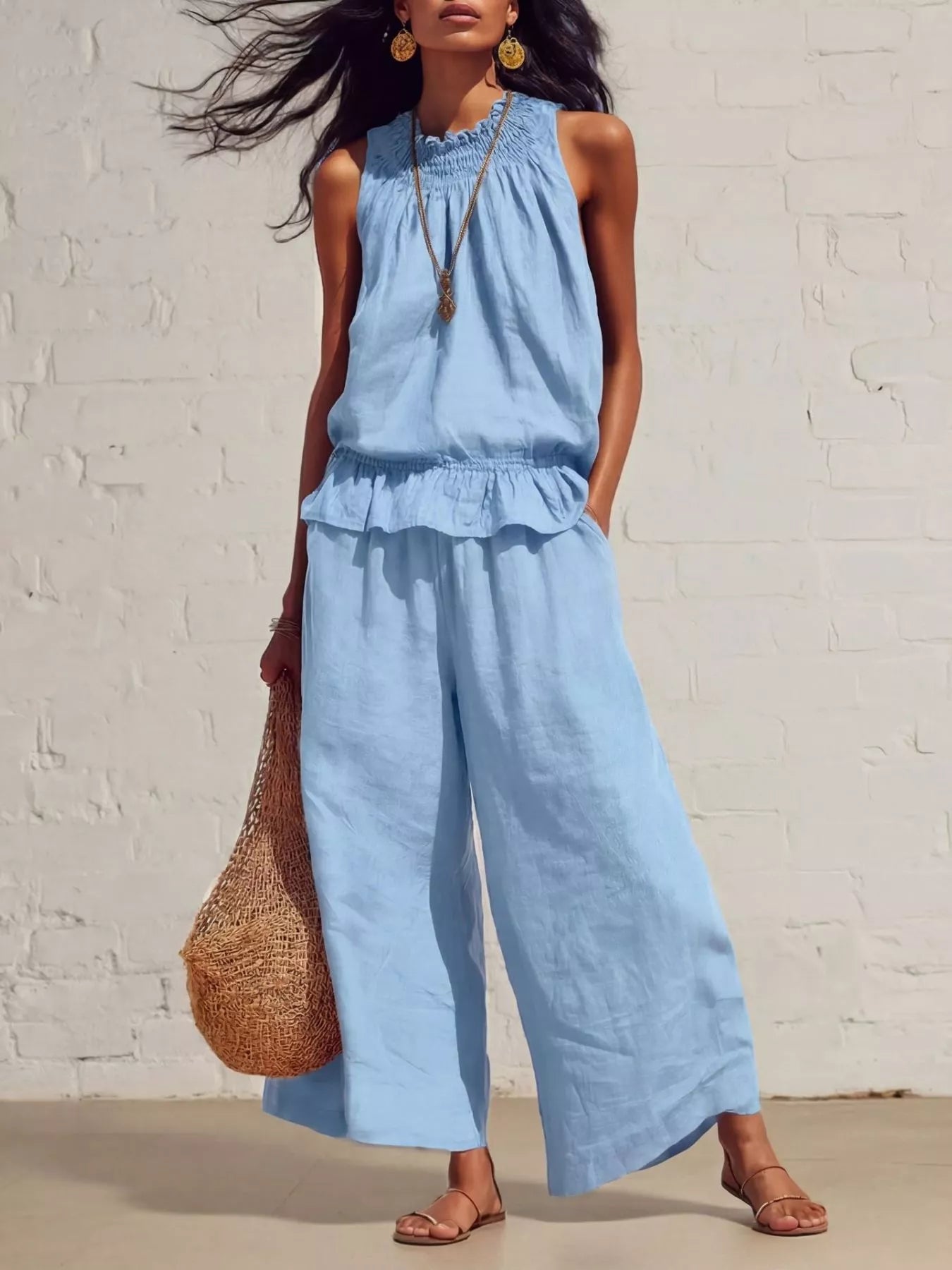 NEWYORKLISTED STYLE COLLECTION: Woman wearing a light blue jumpsuit against a white brick wall.
