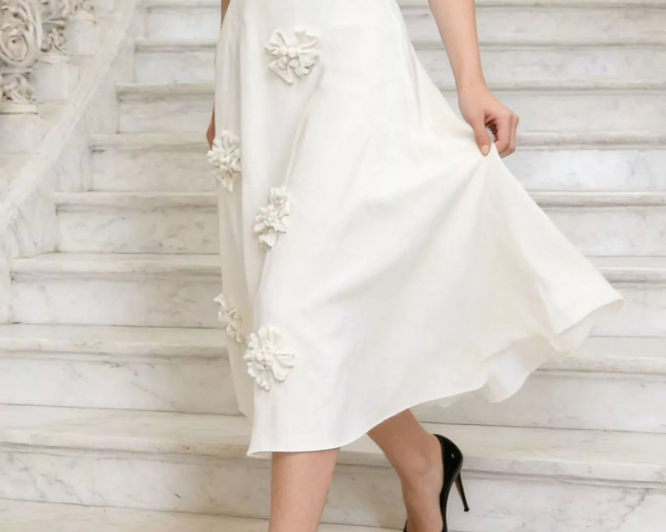 NEWYORKLISTED STYLE COLLECTION: Person wearing a white skirt with floral embellishments on marble stairs