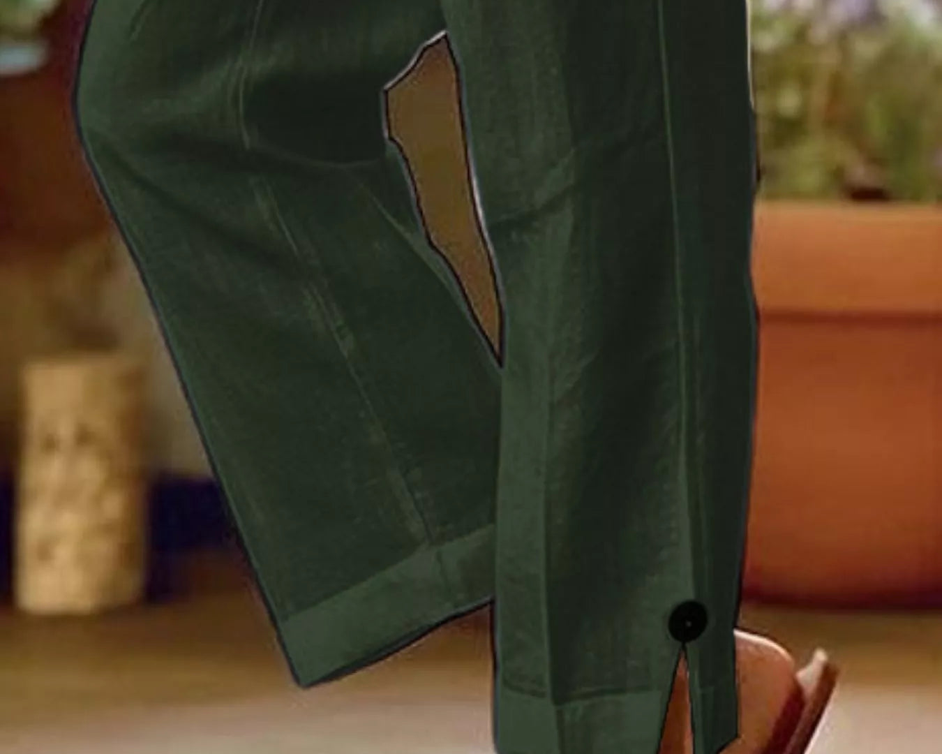 NEWYORKLISTED STYLE COLLECTION: A close-up of a person wearing dark olive green wide-leg pants with a side slit and a small black button detail near the hem, paired with gold-toned slide sandals.