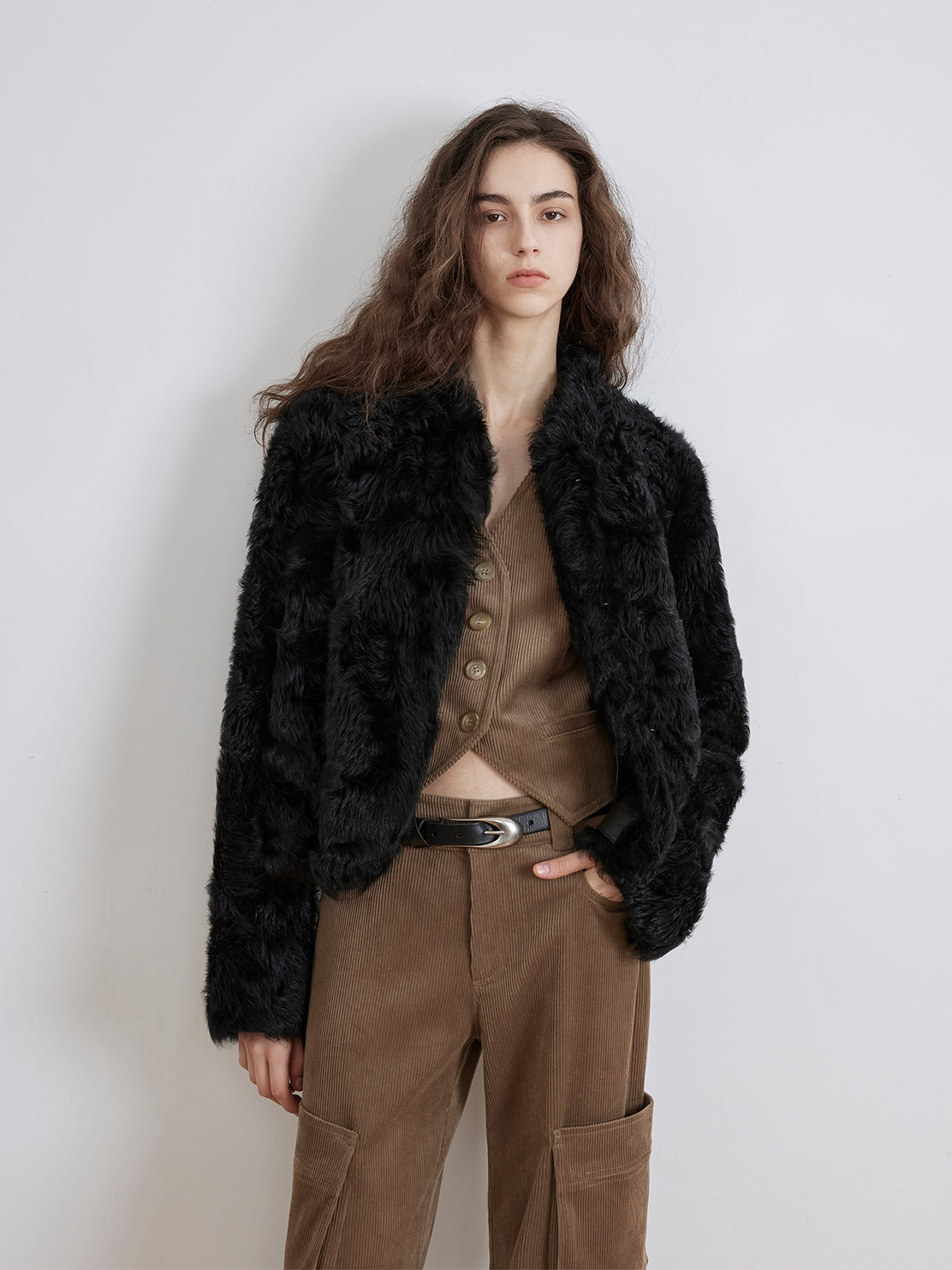 NEWYORKLISTED STYLE COLLECTION: Woman wearing a black fur jacket and brown pants against a white background