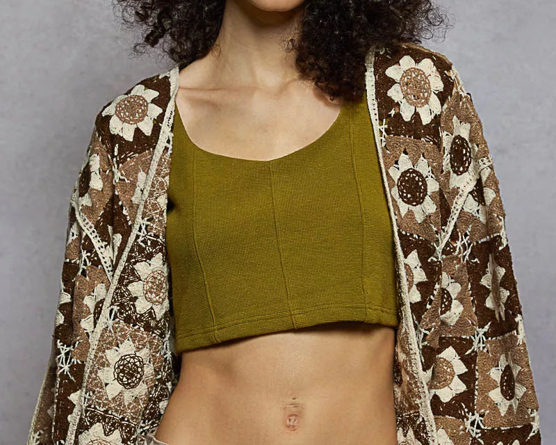 Woman wearing a patterned jacket over a green top and brown pants against a gray background: NEWYORKLISTED STYLE COLLECTION