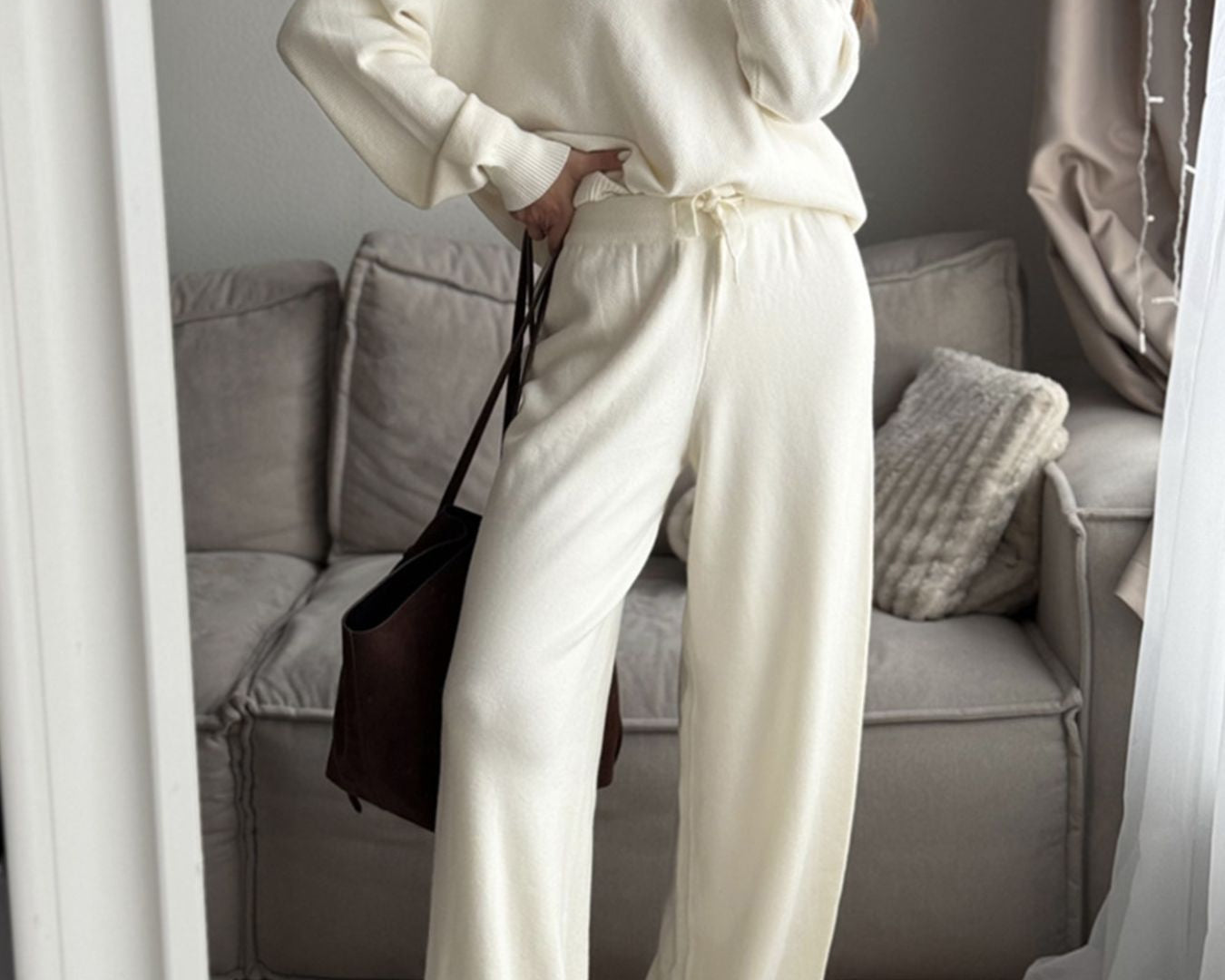 NEWYORKLISTED Comfort Collection: Person wearing a white outfit taking a mirror selfie in a living room.