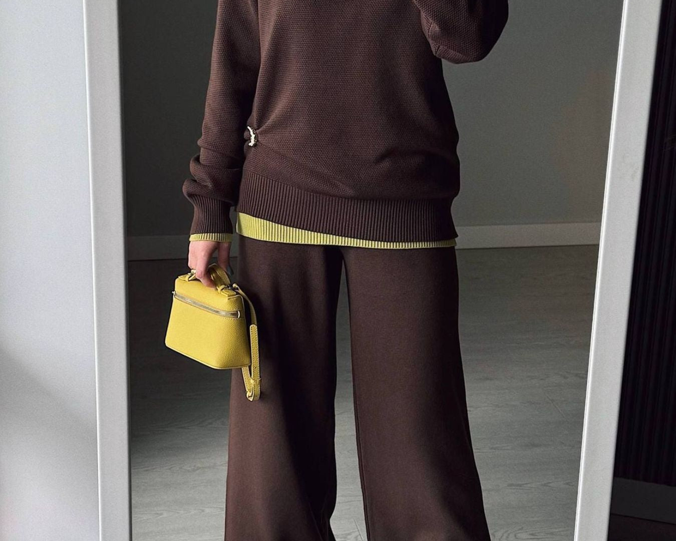 NEWYORKLISTED Comfort Collection: Person wearing a brown outfit with yellow accents, holding a yellow handbag in front of a mirror.