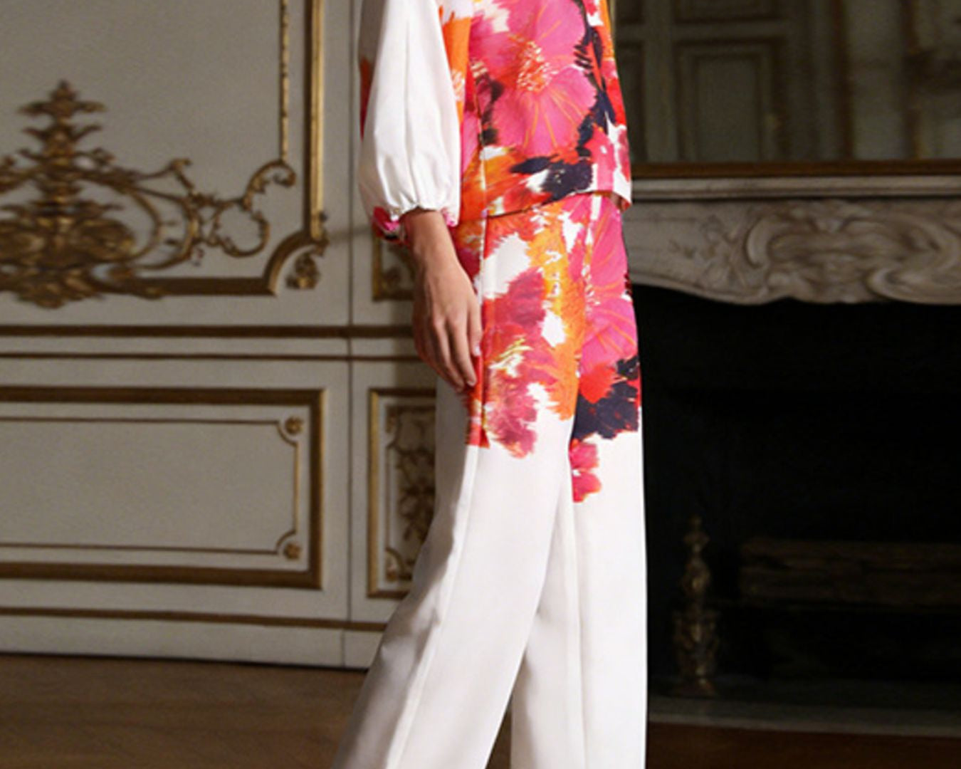 NEWYORKLSITED STYLE COLLECTION: Woman wearing a colorful floral blouse and white pants in an elegant room.