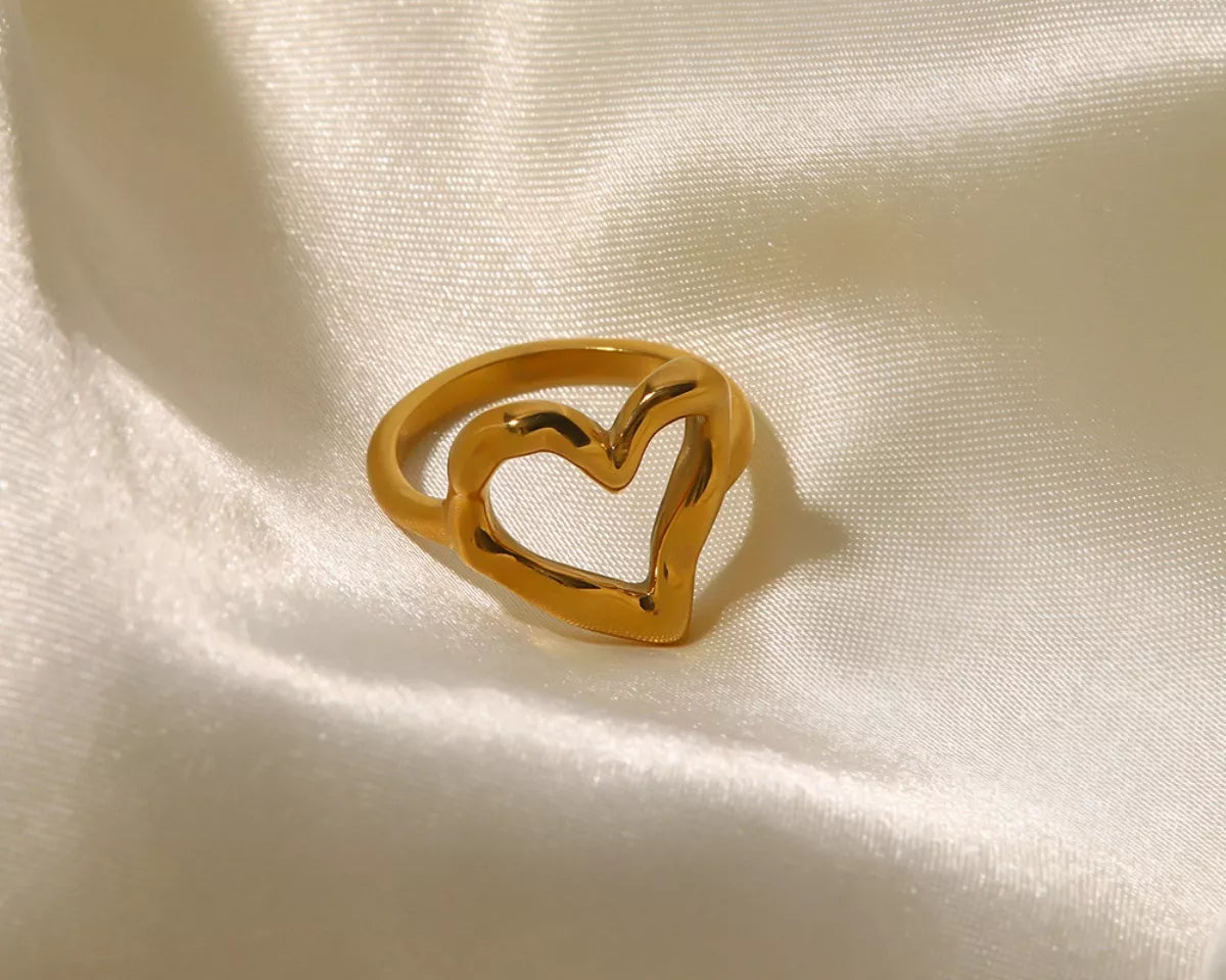 NYLD Glamour Collection by NEWYORKLISTED: Gold heart-shaped ring on a beige fabric background
