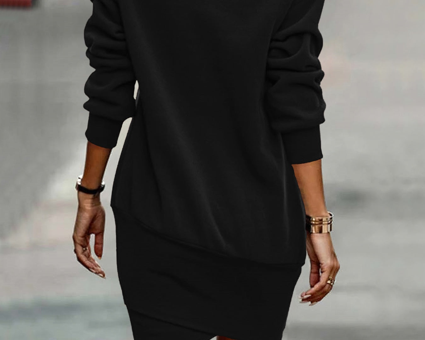 NEWYORKLISTED Style Collection: Person wearing a black dress with long sleeves and an asymmetrical hem, standing on a blurred street background.