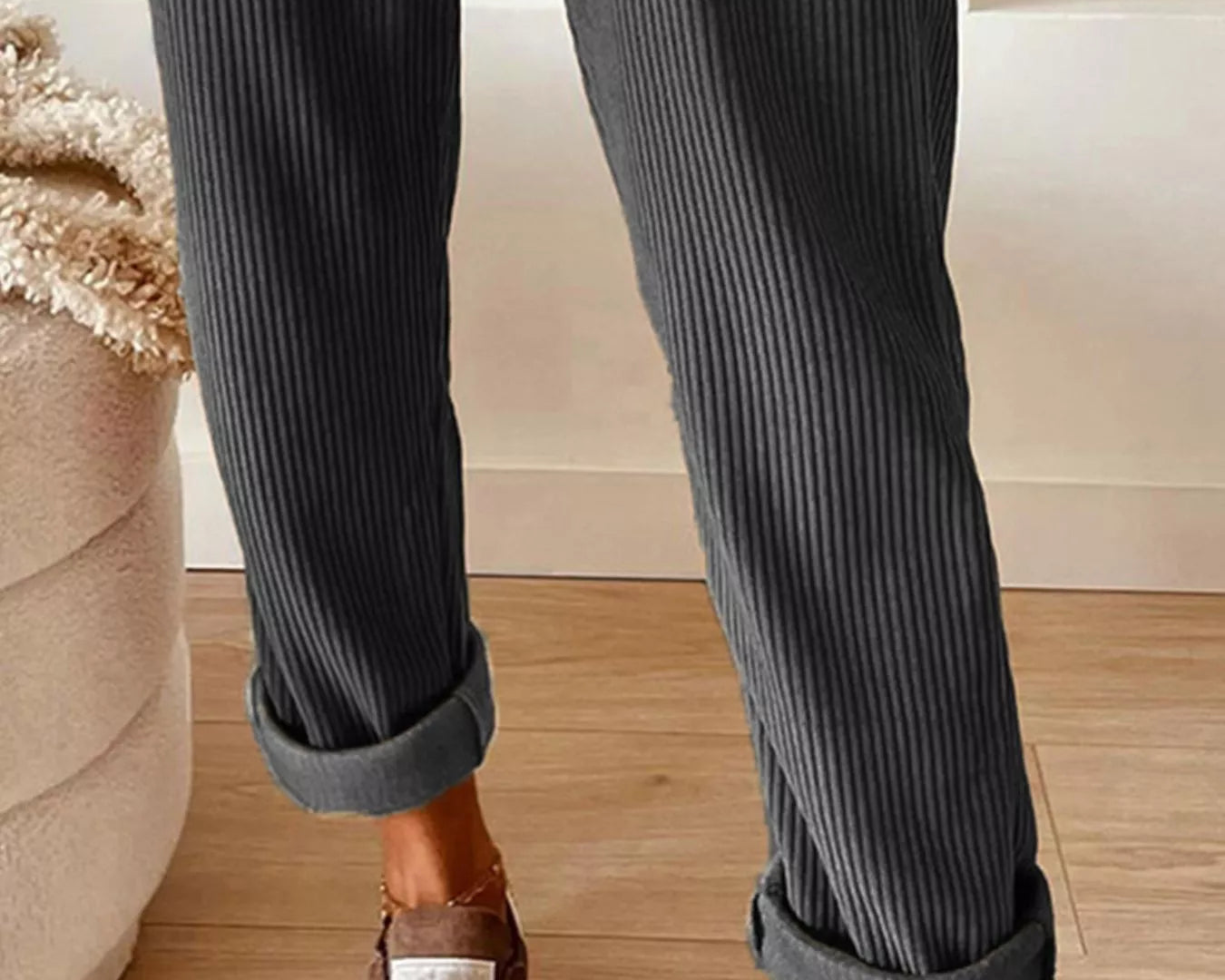 Person wearing dark gray ribbed pants with rolled-up cuffs, standing on a wooden floor.