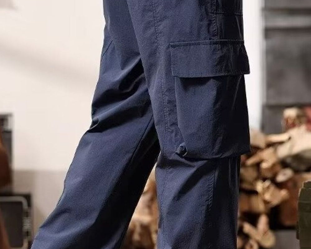 NEWYORKLISTED ATLAS MEN's COLLECTION: Person wearing navy cargo pants in an indoor setting with wooden logs in the background