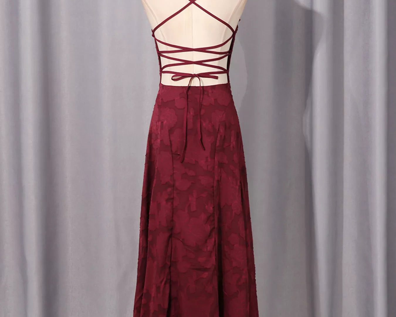 NEWYORKLISTED STYLE COLLECTION: Burgundy dress with criss-cross straps on a mannequin against a gray curtain background