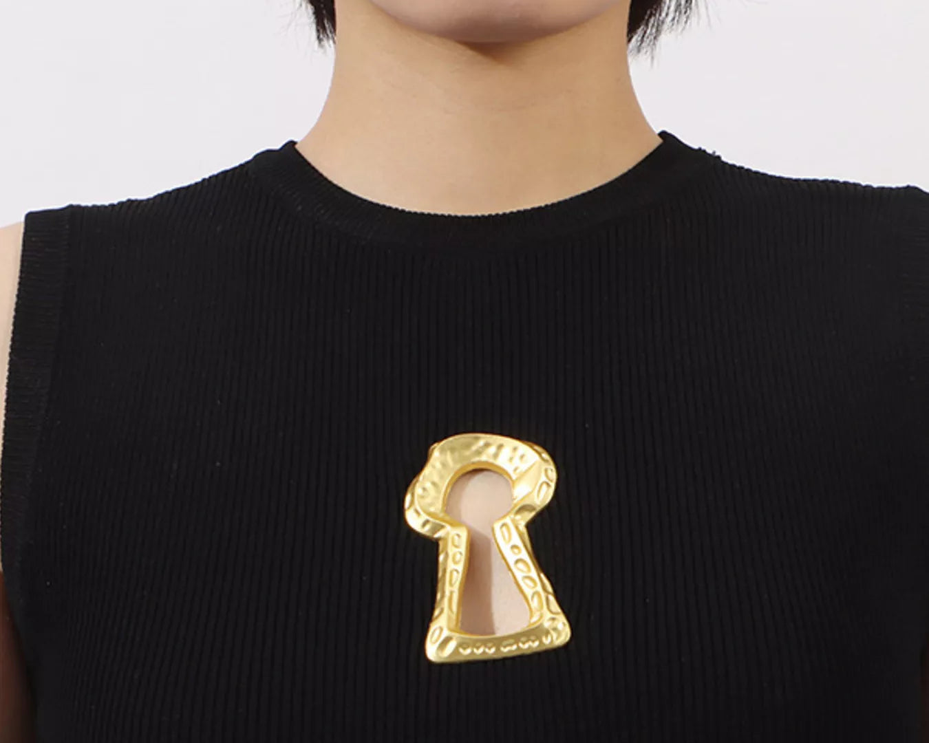 NEWYORKLISTED RUNWAY STYLE: Person wearing a black sleeveless top with a gold keyhole brooch on a white background