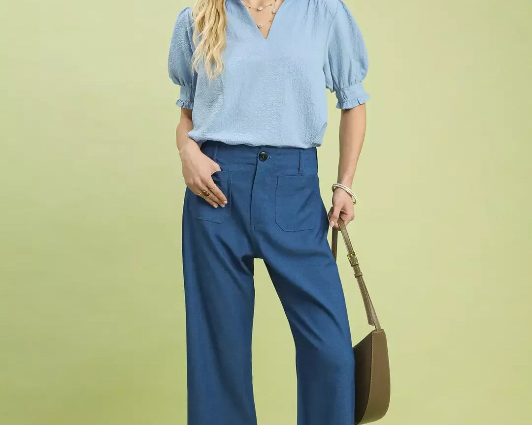 NEWYORKLISTED Style Collection: Woman wearing a blue blouse and pants with a brown handbag on a light green background