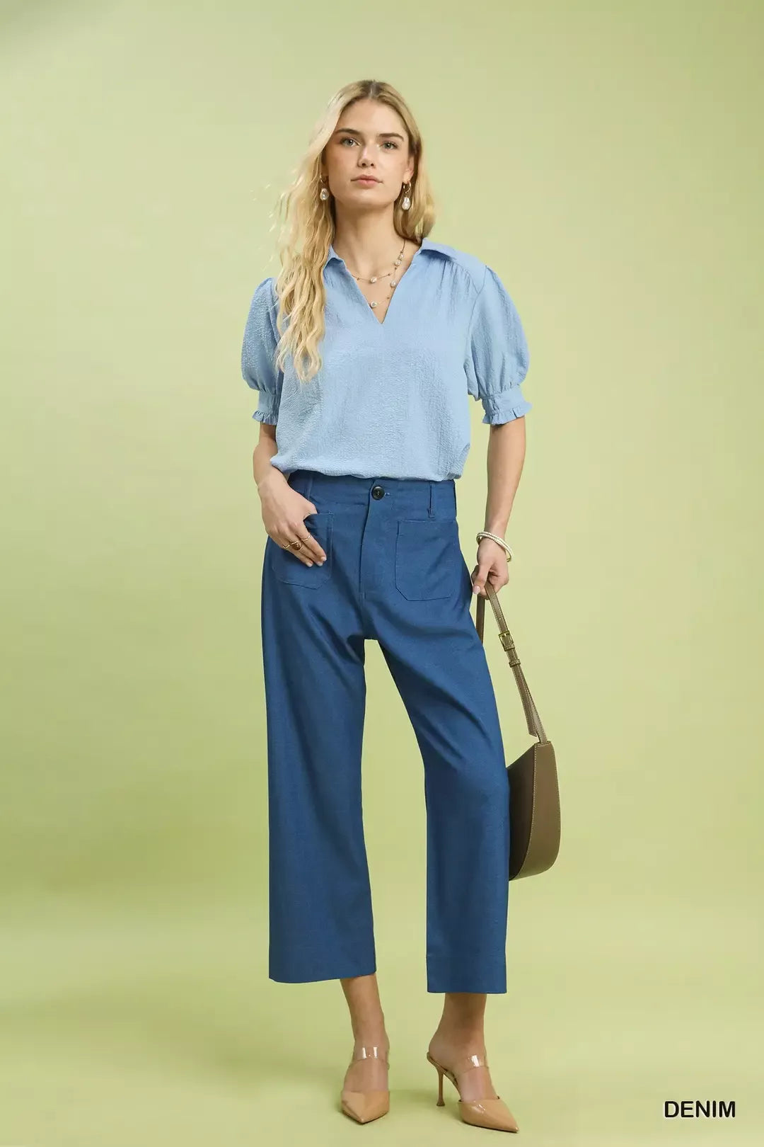 NEWYORKLISTED Style Collection: Woman wearing a blue blouse and pants with a brown handbag on a light green background