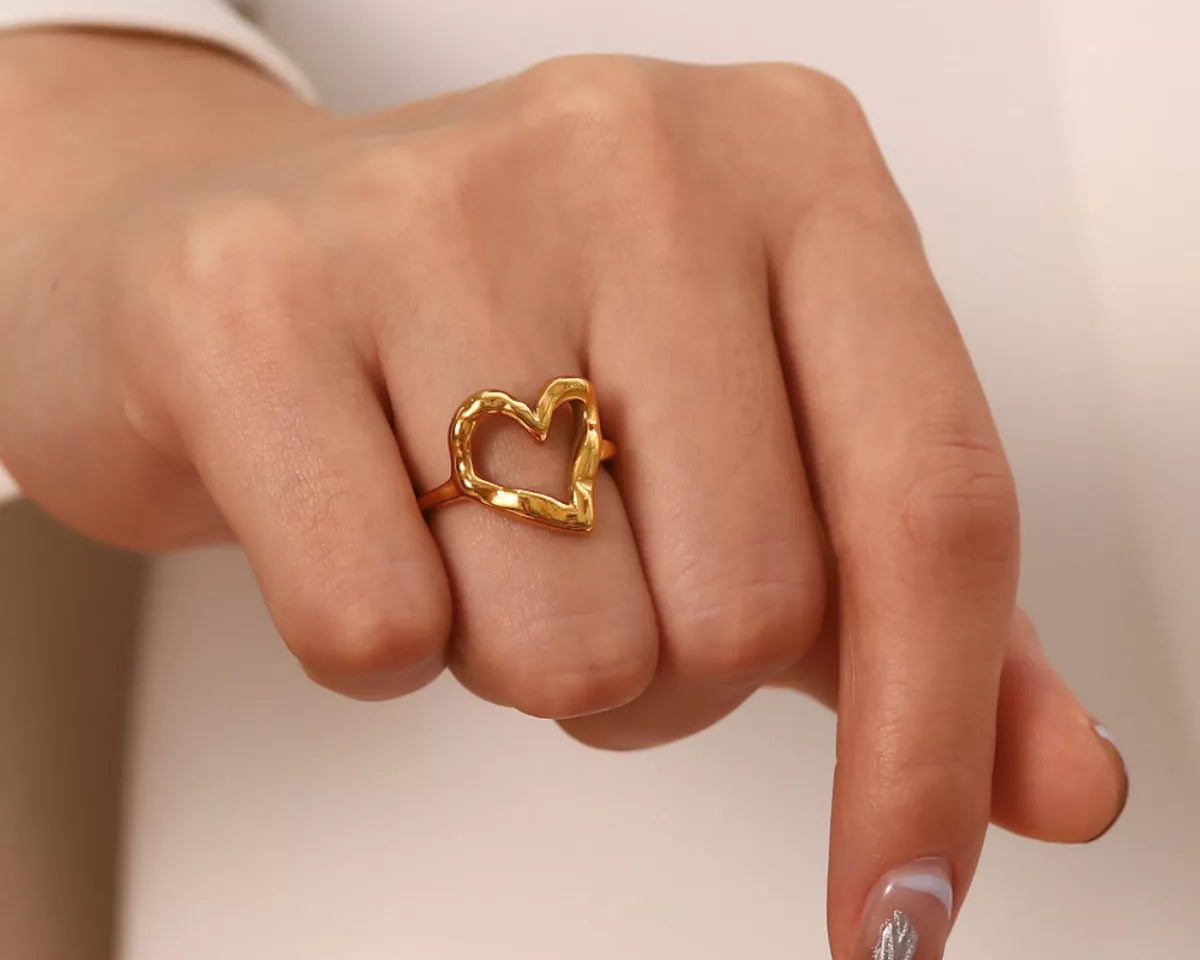 NYLD Glamour Collection by NEWYORKLISTED: Gold heart-shaped ring on a finger against a neutral background