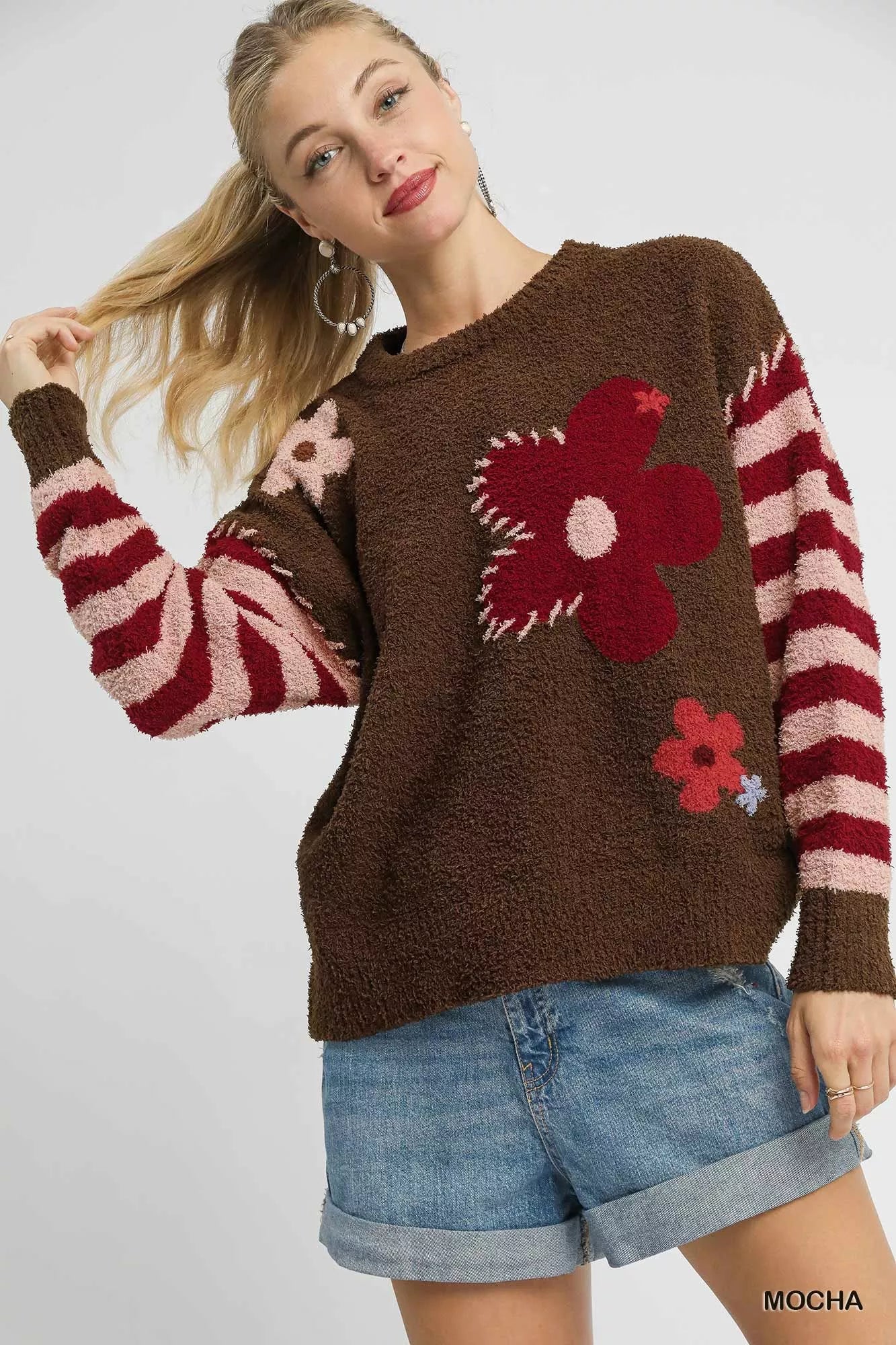 NEWYORKLISTED STYLE COLLECTION: Woman wearing a brown sweater with floral patterns and striped sleeves on a white background