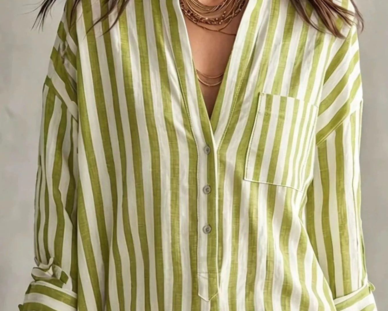 NEWYORKLISTED STYLE COLLECTION: A woman wearing a light green and white vertically striped button-up shirt with a chest pocket, styled with layered gold necklaces and earrings.