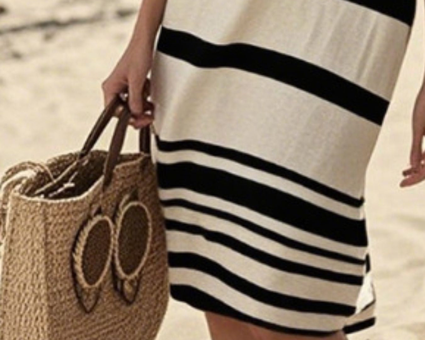 NEWYORKLISTED STYLE COLLECTION: Person wearing a black and white striped dress holding a woven bag on a beach.