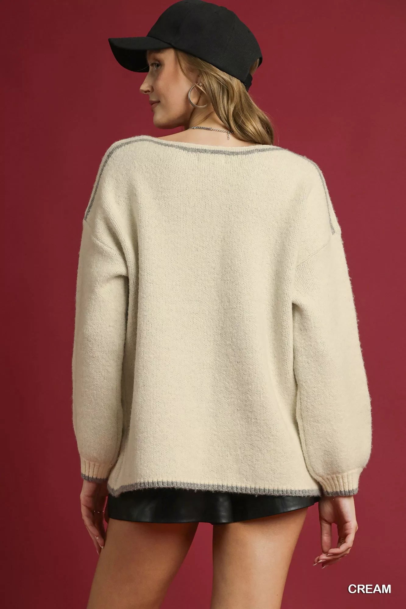 NEWYORKLISTED STYLE COLLECTION: Woman wearing a cream sweater and black cap on a red background