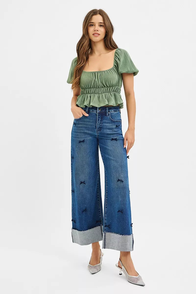 NEWYORKLISTED STYLE COLLECTION: Woman wearing a green top and blue jeans with distressed details on a white background