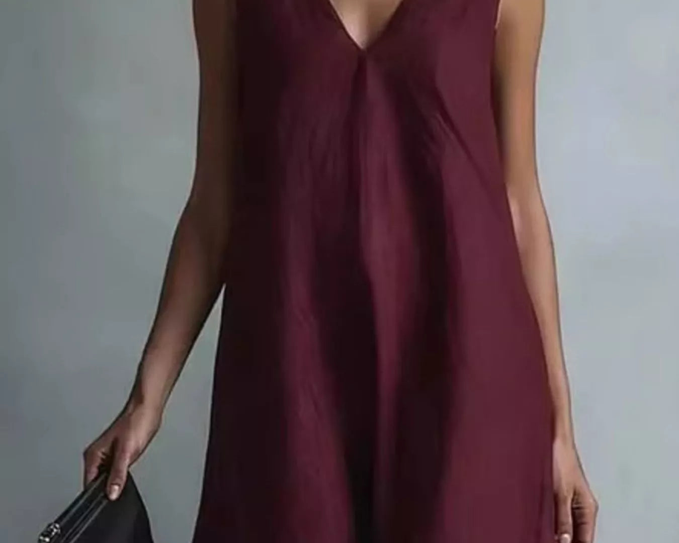 NEWYORKLISTED STYLE COLLECTION: A woman wearing a sleeveless deep burgundy V-neck maxi dress, holding a small black leather clutch against a neutral gray studio background.