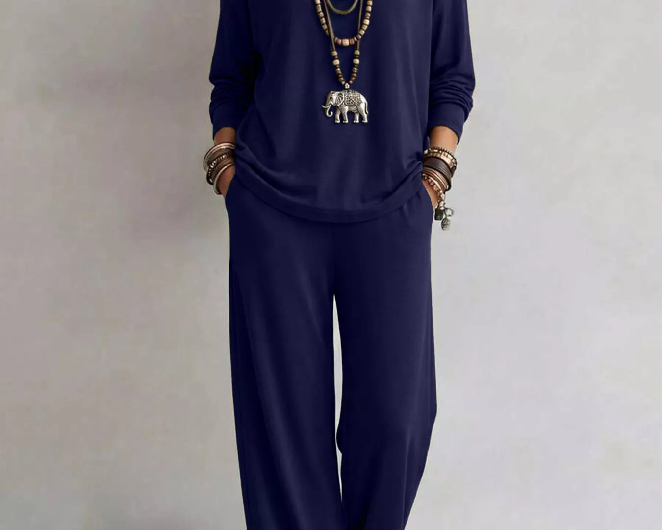 NEWYORKLISTED STYLE COLLECTION: A woman modeling a navy blue two-piece lounge set consisting of a long-sleeve top and matching wide-leg pants, styled with layered gold necklaces and bracelets against a neutral studio background.