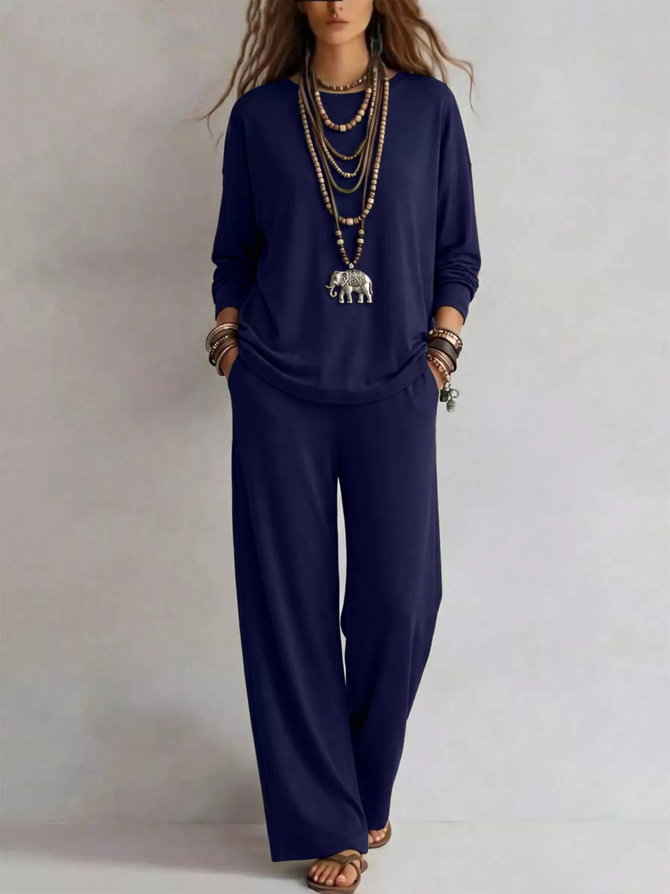 NEWYORKLISTED STYLE COLLECTION: A woman modeling a navy blue two-piece lounge set consisting of a long-sleeve top and matching wide-leg pants, styled with layered gold necklaces and bracelets against a neutral studio background.