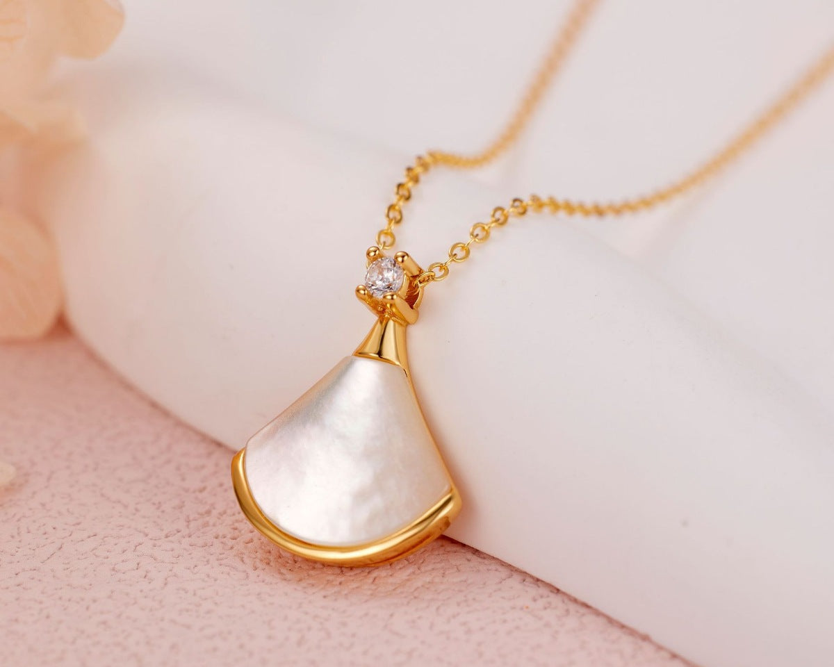 NYLD Glamour By NEWYORKLISTED: Gold necklace with a white pendant on a soft pink background
