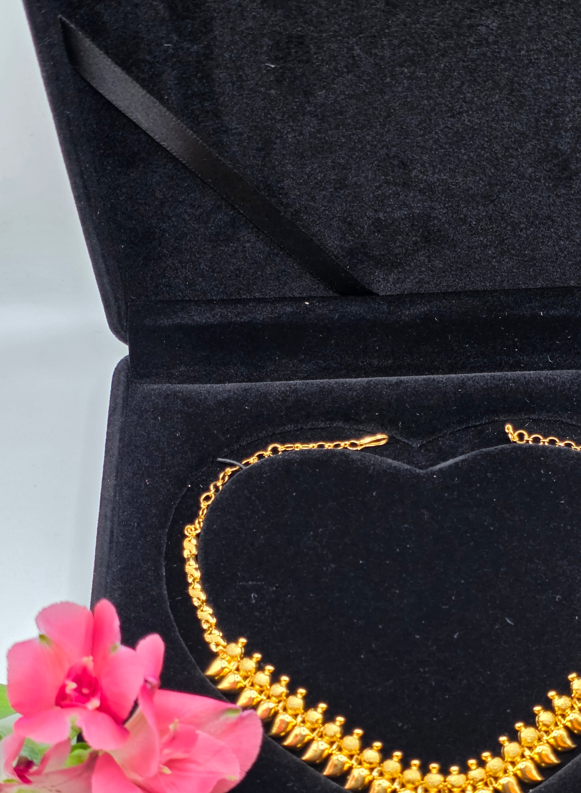 NEWYORKLISTED: 22k Gold necklace in a black jewelry box with flowers on a light background