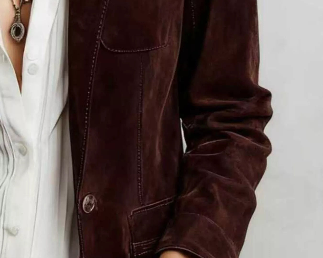 NEWYORKLISTED STYLE COLLECTION: A close-up of a person wearing a dark brown suede or velvet jacket over a white button-up shirt and dark jeans, accessorized with layered necklaces.