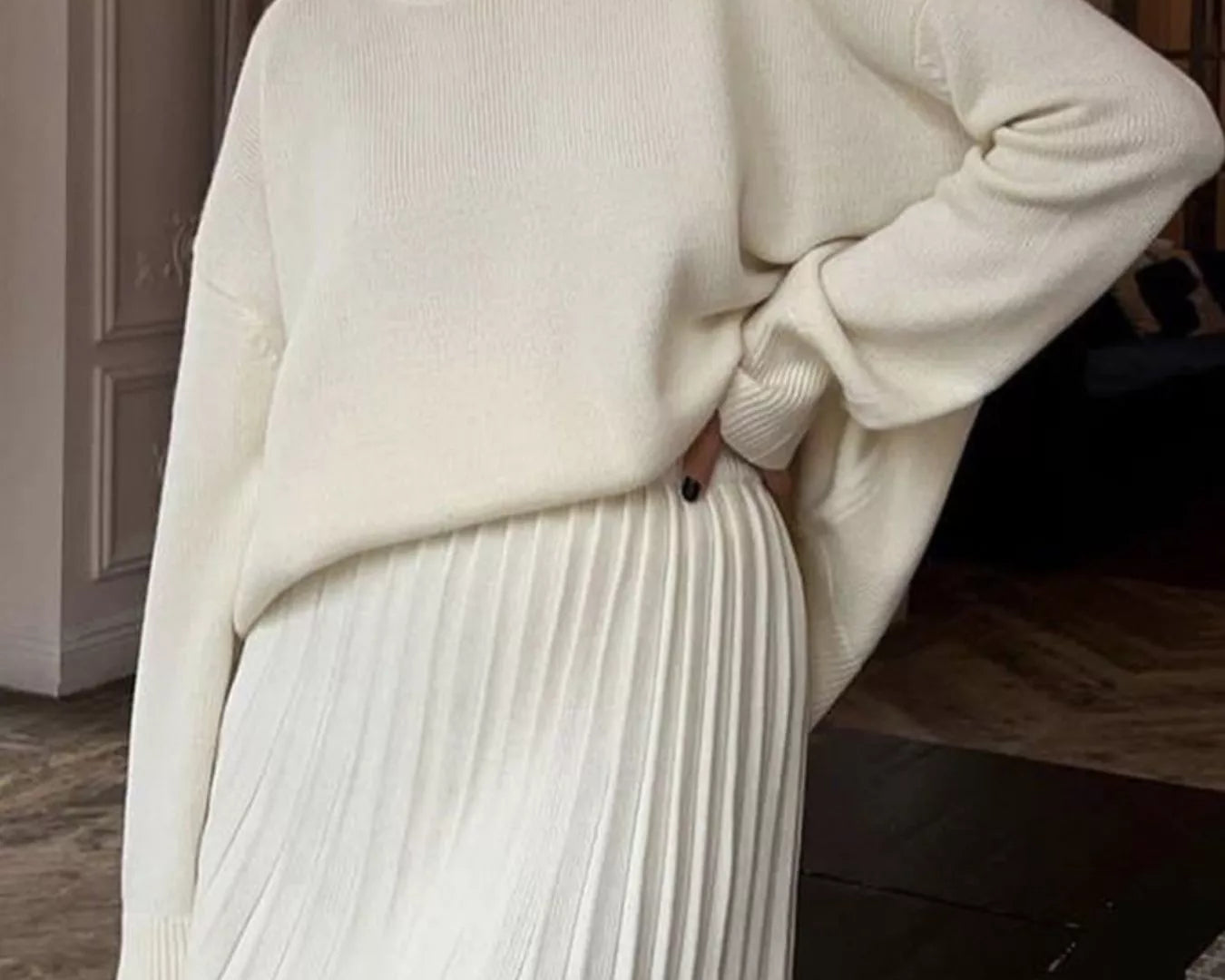 NEWYORKLISTED STYLE COLLECTION: Person wearing a cream sweater and white pleated skirt indoors.