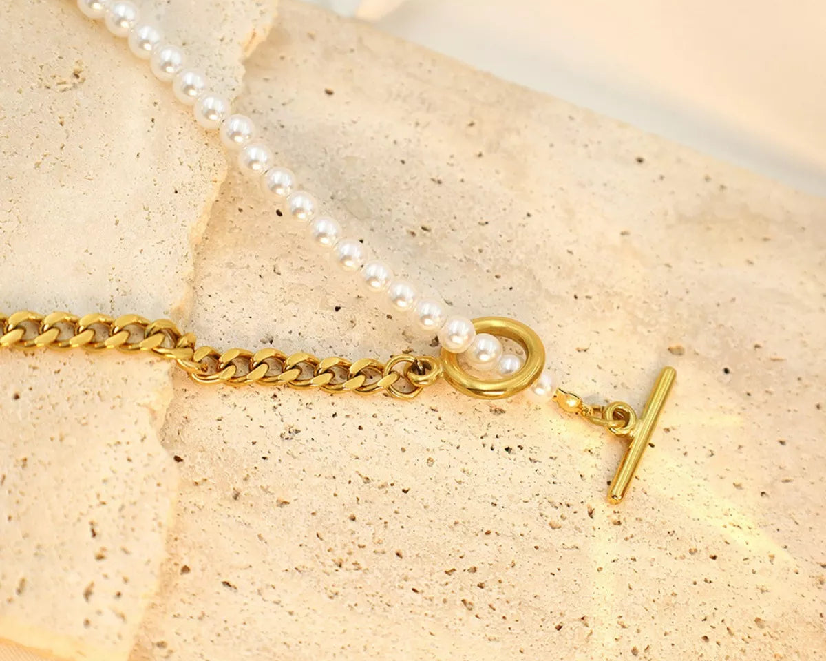 Gold bracelet with a pearl charm on a beige stone surface