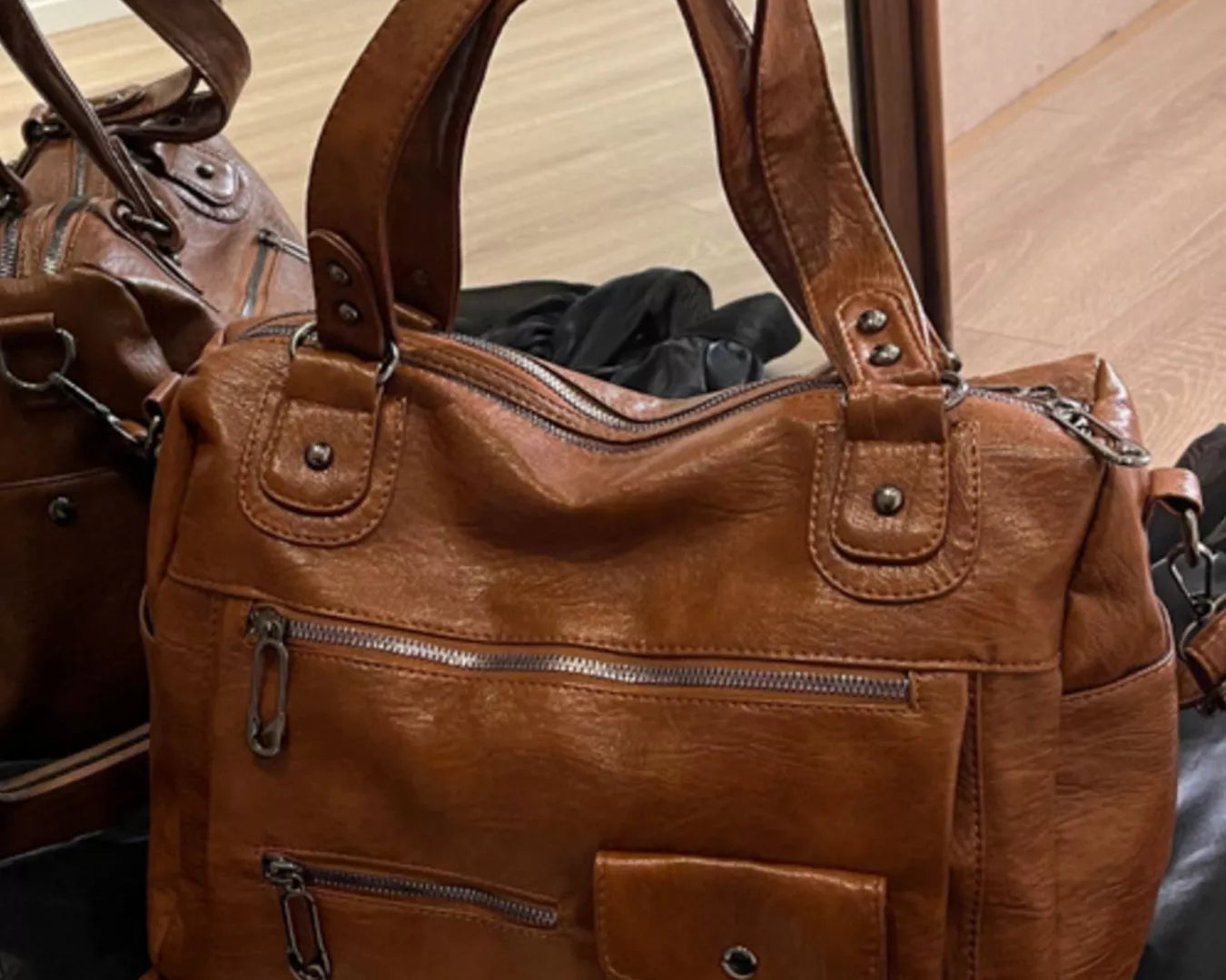 NEWYORKLISTED STYLE COLLECTION: Brown leather handbag with multiple pockets and zippers on a surface.