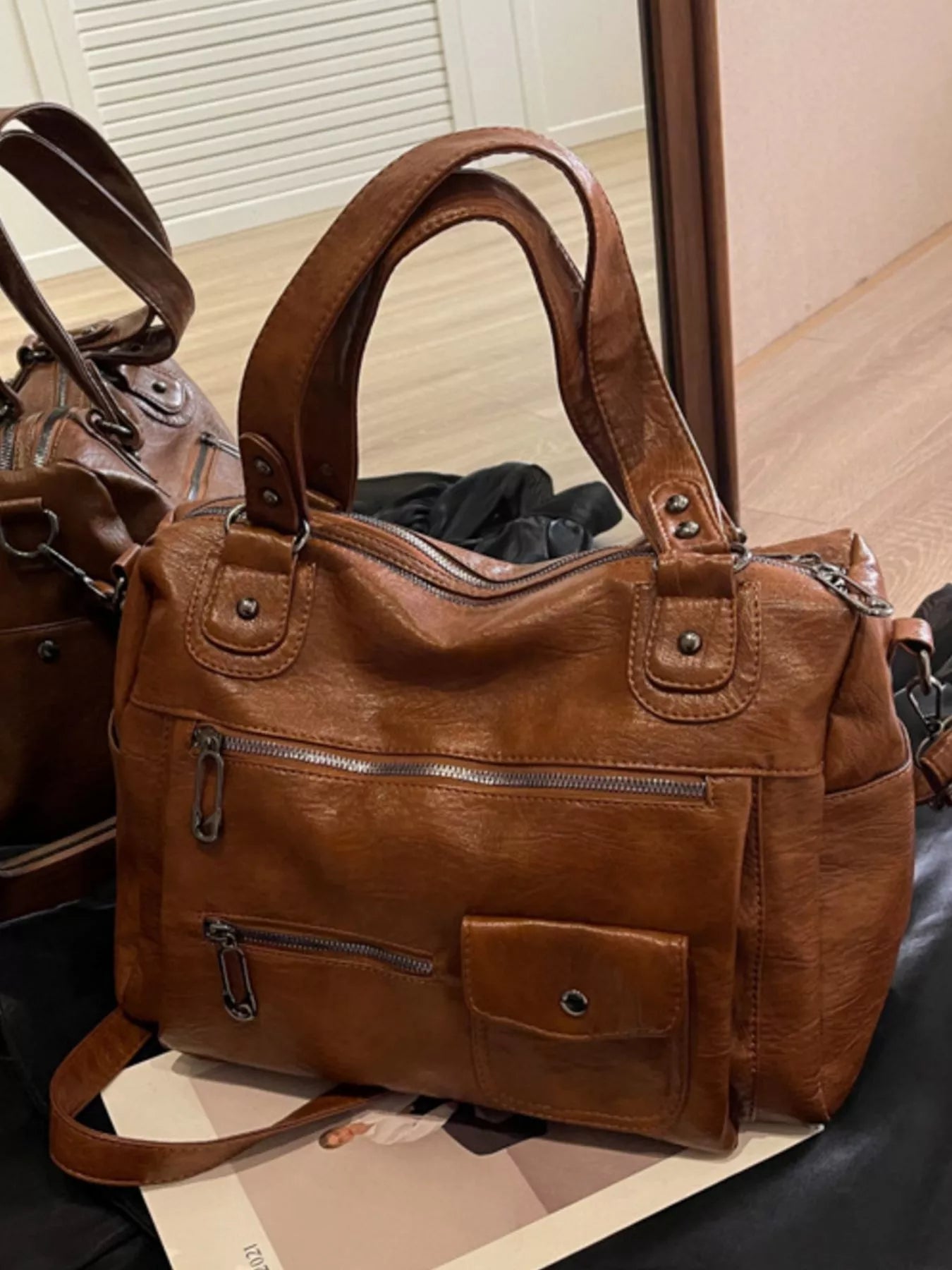 NEWYORKLISTED STYLE COLLECTION: Brown leather handbag with multiple pockets and zippers on a surface.