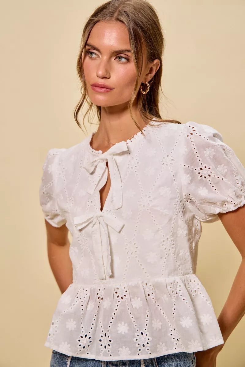 NEWYORKLISTED STYLE COLLECTION: Woman wearing a white lace blouse with puff sleeves against a beige background