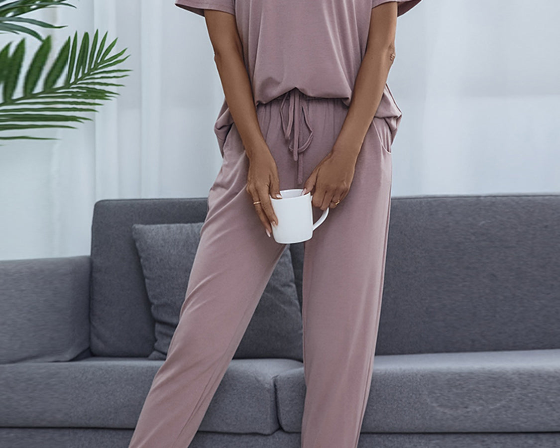 NEWYORKLISTED Intimate Apparel: Person wearing a mauve pajama set sitting on a gray couch with a plant in the background