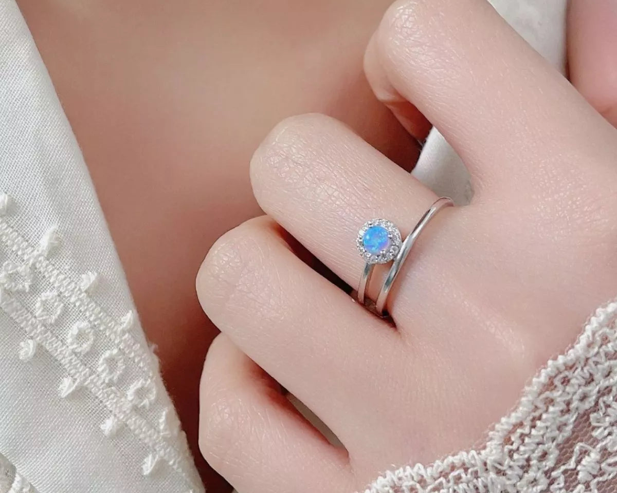 NYLD Glamour Collection by NEWYORKLISTED: Close-up of a hand wearing a silver ring with a blue gemstone, against a soft background.