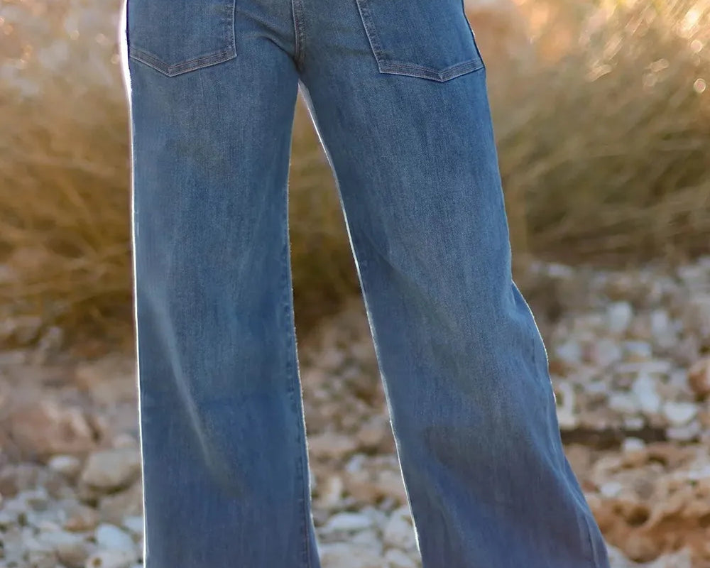 NEWYORKLISTED STYLE COLLECTION: Person wearing blue flared jeans standing on a rocky surface with a blurred natural background