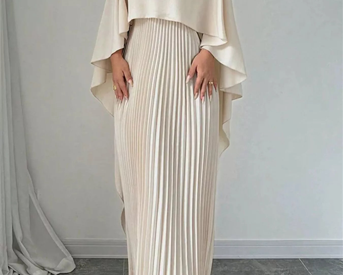 NEWYORKLISTED STYLE COLLECTION: Woman wearing a beige pleated dress with a matching top against a plain background