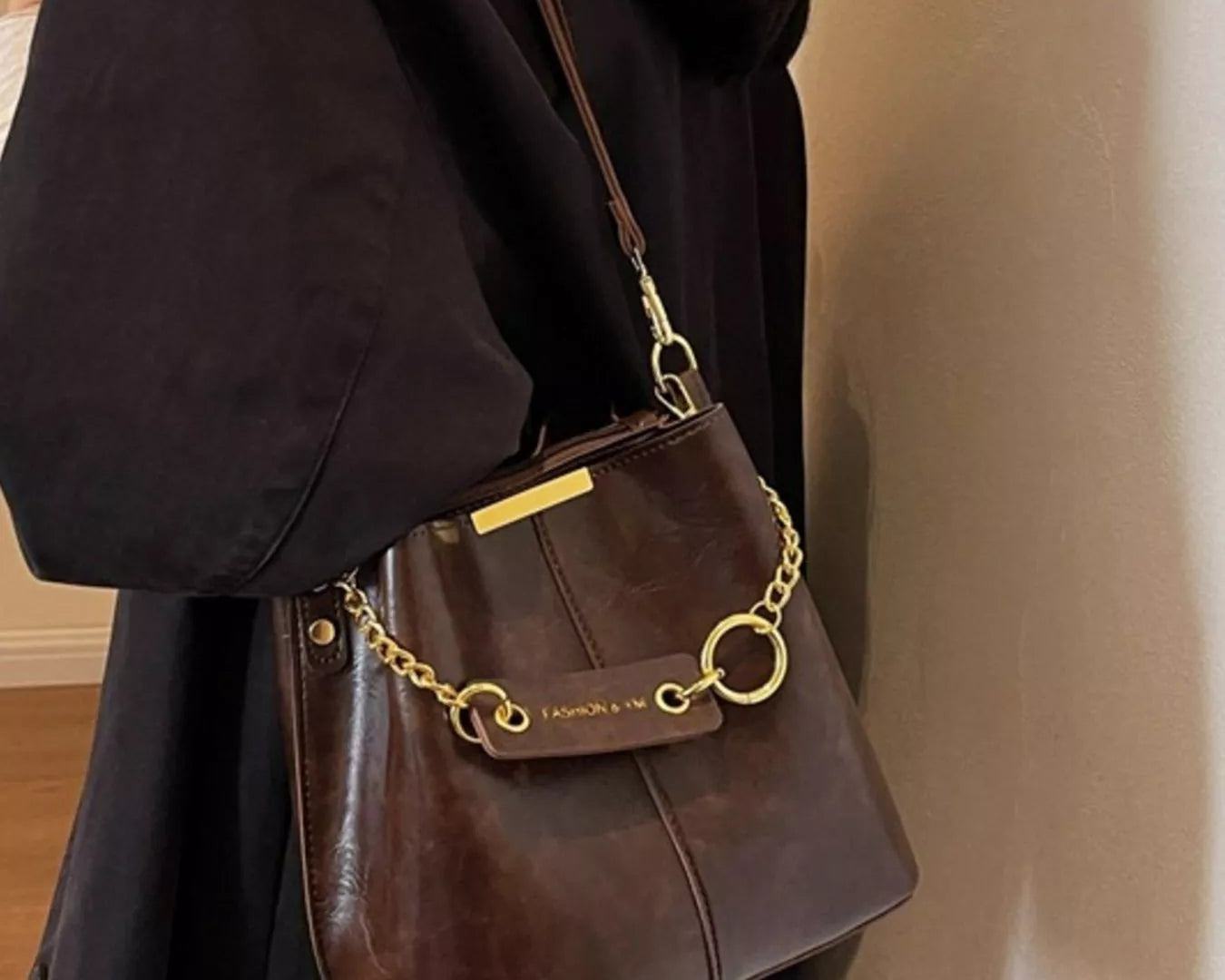 Brown handbag with gold chain strap held by a person wearing a black coat.