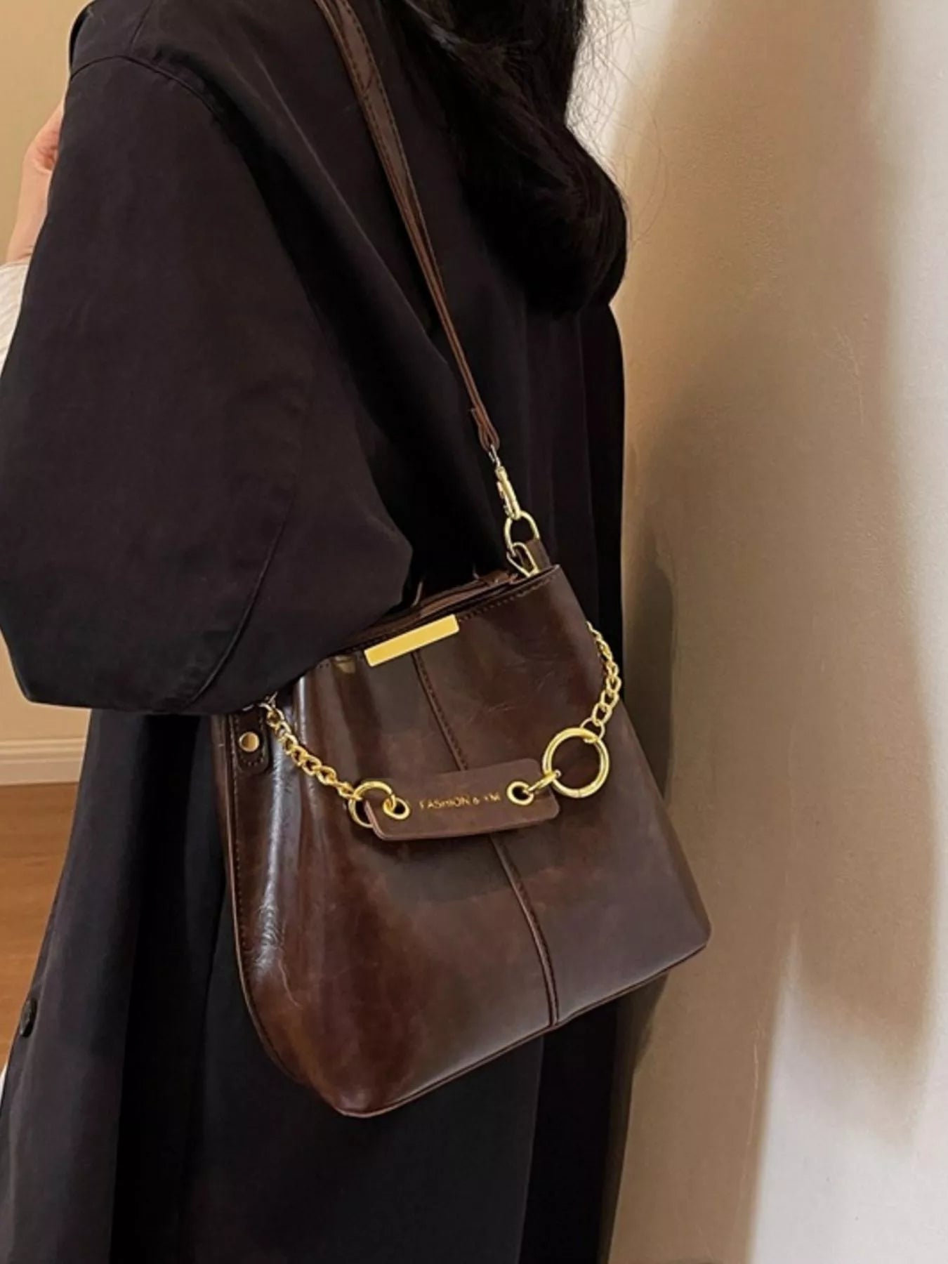 Brown handbag with gold chain strap held by a person wearing a black coat.