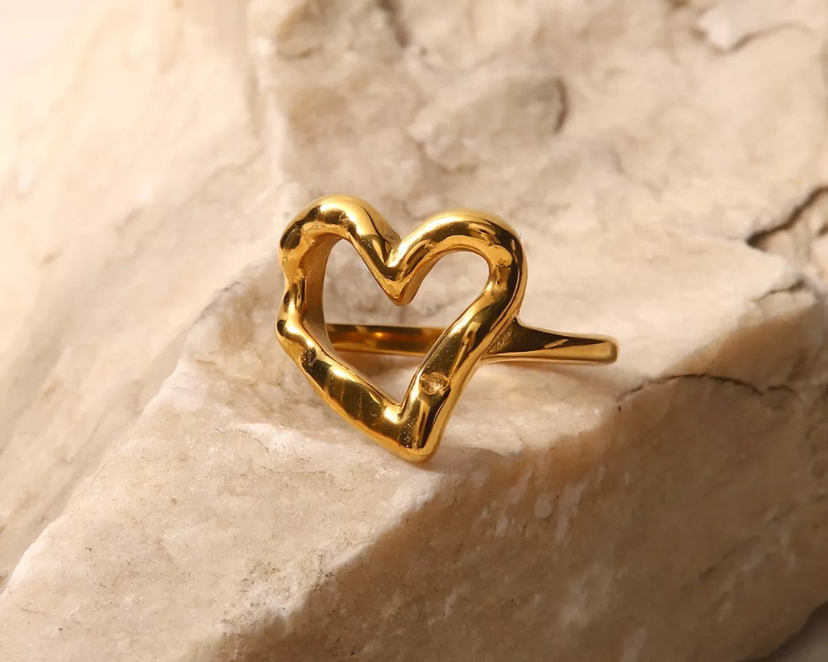 NYLD Glamour Collection by NEWYORKLISTED: Gold heart-shaped ring on a textured beige surface