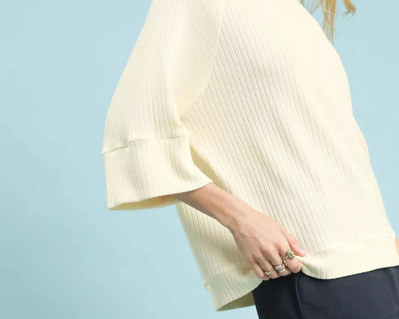 NEWYORKLISTED STYLE COLLECTION: Woman wearing a light-colored top and dark shorts against a light blue background