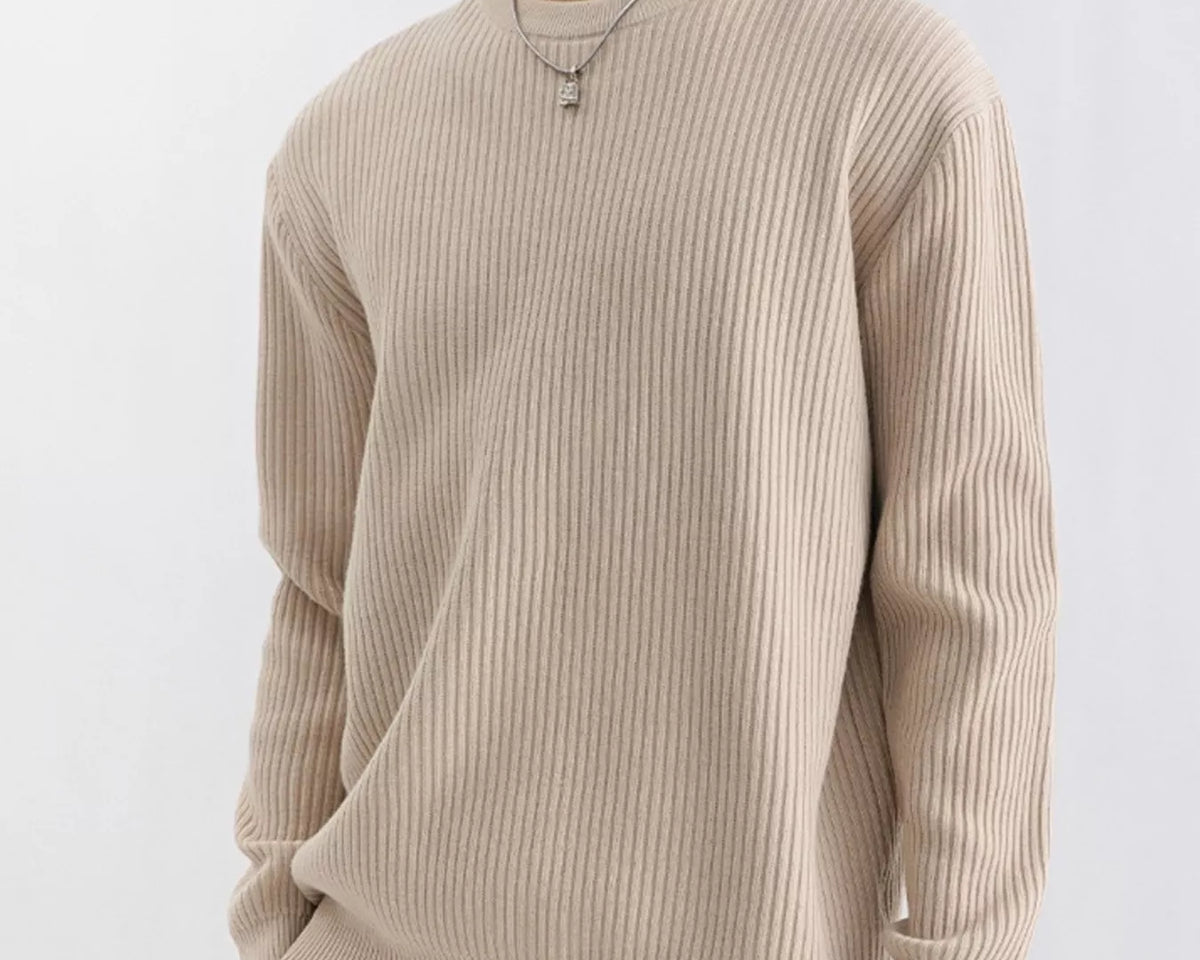 NEWYORKLISTED ATLAS MEN'S COLLECTION: A man wearing a beige ribbed long-sleeve crewneck sweater and tan pants, photographed against a clean light gray studio background.