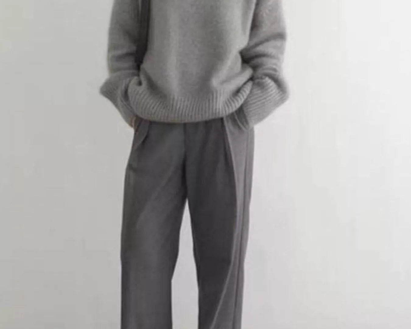 Person wearing a gray sweater and pants against a white background