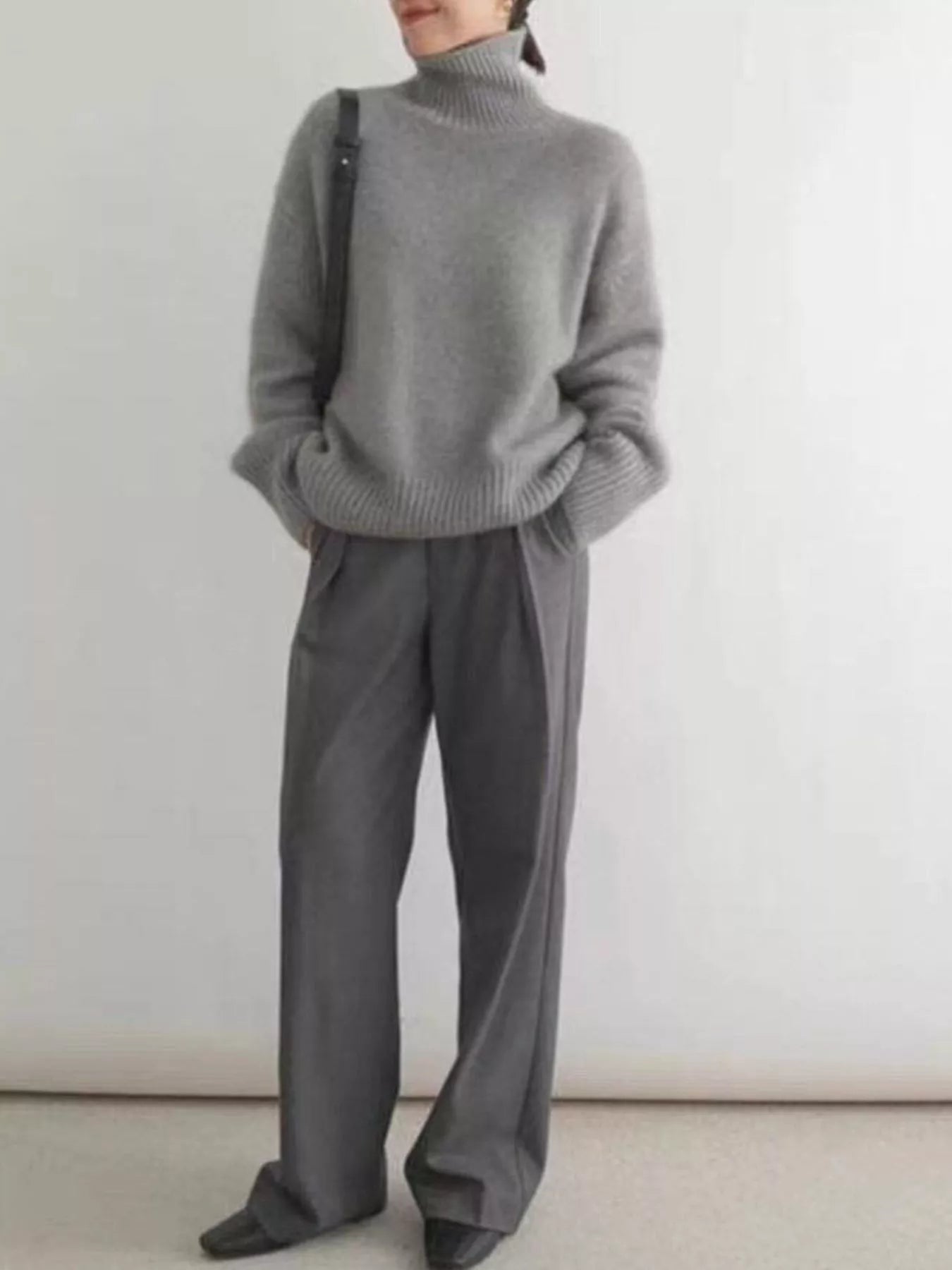 Person wearing a gray sweater and pants against a white background