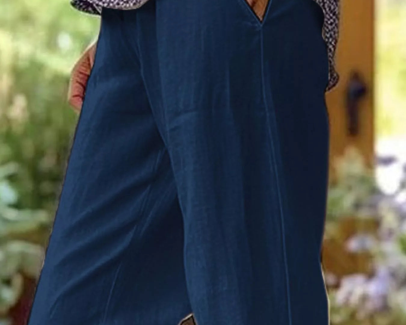 NEWYORKLISTED STYLE COLLECTION: A person wearing loose, wide-leg navy blue pants with a patterned top and a gold watch, standing in a softly blurred outdoor setting.