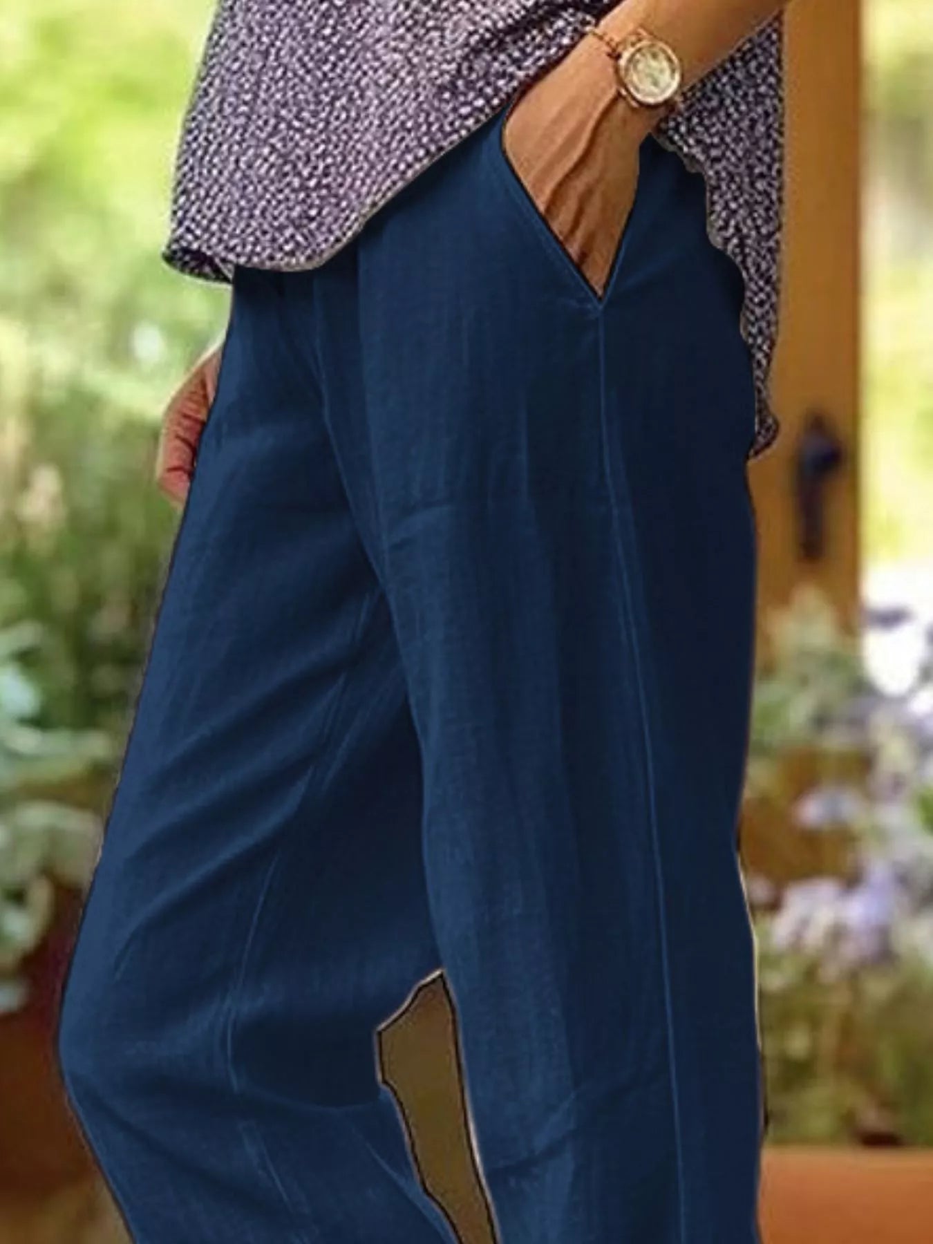 NEWYORKLISTED STYLE COLLECTION: A person wearing loose, wide-leg navy blue pants with a patterned top and a gold watch, standing in a softly blurred outdoor setting.